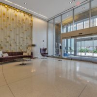 A modern hotel lobby features a large glass entrance, a polished floor, and a gold-accented wall. It is furnished with a brown sofa, chairs, and sleek lighting, creating an inviting atmosphere.